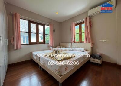 Bedroom with wooden flooring, a large bed, and windows with pink curtains