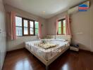 Bedroom with wooden flooring, a large bed, and windows with pink curtains