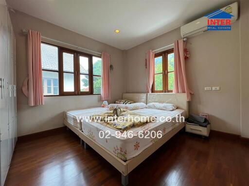 Bedroom with wooden flooring, a large bed, and windows with pink curtains