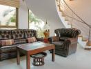 Cozy living room with brown leather furniture and a staircase