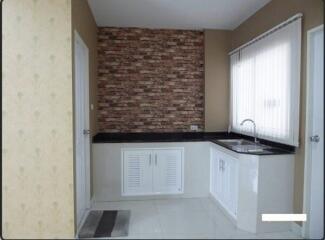 Small modern kitchen with brick accent wall, white cabinets, and a window