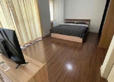 Spacious bedroom with wooden floor, large bed, television, and ample natural light