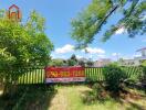 Front yard with a fence and a for sale sign, surrounded by greenery