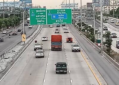 View of a busy highway with multiple lanes and vehicles, and road signs in both English and Thai.