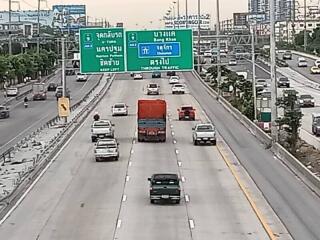 View of a busy highway with multiple lanes and vehicles, and road signs in both English and Thai.