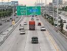 View of a busy highway with multiple lanes and vehicles, and road signs in both English and Thai.