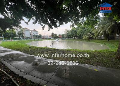 View of a pond in a residential area surrounded by trees with a path in the foreground