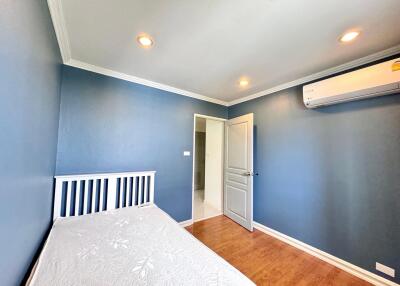 Small bedroom with blue walls, white bed frame, wooden floor, and air conditioning unit