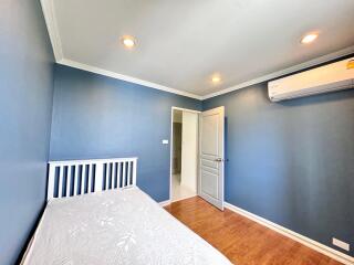 Small bedroom with blue walls, white bed frame, wooden floor, and air conditioning unit