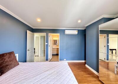 Spacious bedroom with blue walls, a bed with a white comforter, a mirror, and wood flooring