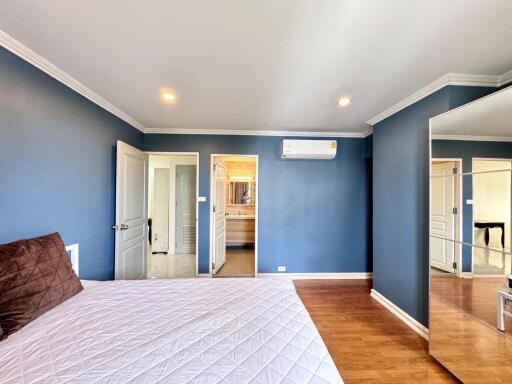 Spacious bedroom with blue walls, a bed with a white comforter, a mirror, and wood flooring