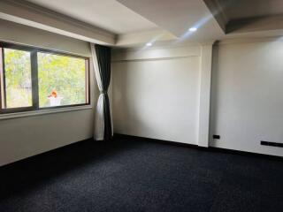 Spacious empty living room with large window and dark carpet