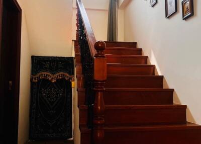 A wooden staircase leading to an upper floor with a high window and framed pictures on the wall.