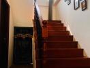 A wooden staircase leading to an upper floor with a high window and framed pictures on the wall.