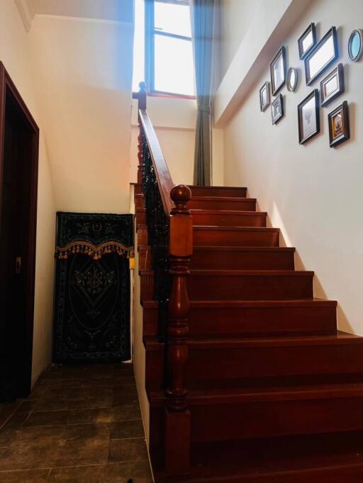 A wooden staircase leading to an upper floor with a high window and framed pictures on the wall.