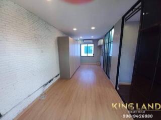 spacious modern bedroom with wooden flooring, white brick walls, built-in wardrobe, and large window