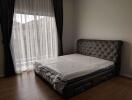 Bedroom with a large bed, headboard, and floor-to-ceiling window with curtains