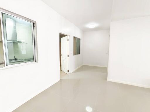 Empty room with white walls and doors, adjacent to kitchen