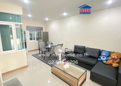 Cozy living room with a black sectional sofa, a glass coffee table, and a dining area in the background