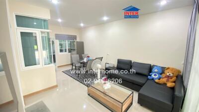 Cozy living room with a black sectional sofa, a glass coffee table, and a dining area in the background