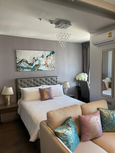 Modern bedroom with a bed, decorative pillows, bedside tables, wall art, air conditioning, and a desk with a chair