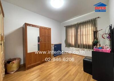 A bedroom with wooden floor, a window with curtains, and a wooden wardrobe.