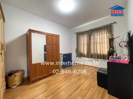 A bedroom with wooden floor, a window with curtains, and a wooden wardrobe.