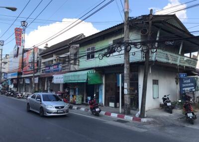 Street view of a residential area with shops, motorcycles, and cars.