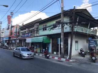 Street view of a residential area with shops, motorcycles, and cars.