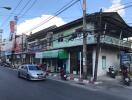 Street view of a residential area with shops, motorcycles, and cars.