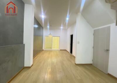 Spacious living room with wooden flooring, ceiling lights, and adjacent hallway.