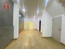 Spacious living room with wooden flooring, ceiling lights, and adjacent hallway.