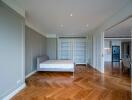 Spacious bedroom with wooden flooring and large bed, featuring built-in shelves and a view towards the kitchen area.