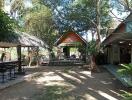 Exterior view of a property with a shaded outdoor area, a hut, and lush greenery.