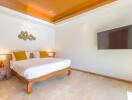 Modern bedroom with a wooden bed frame, wall-mounted TV, and large bed with yellow pillows