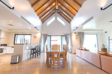 Spacious and modern open-plan living area with high wooden ceiling, dining table, kitchen and sitting area