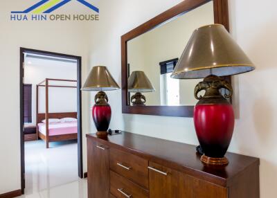 Hallway with dresser, lamps, and mirror leading to bedroom