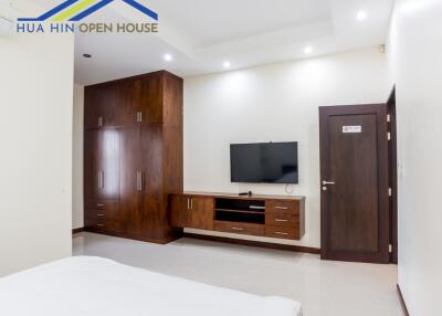 Bedroom with wooden furniture, wall-mounted TV, and white walls