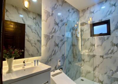 Modern bathroom with marble walls, illuminated mirror, vanity, toilet, and glass-enclosed shower