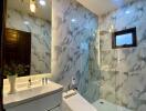 Modern bathroom with marble walls, illuminated mirror, vanity, toilet, and glass-enclosed shower