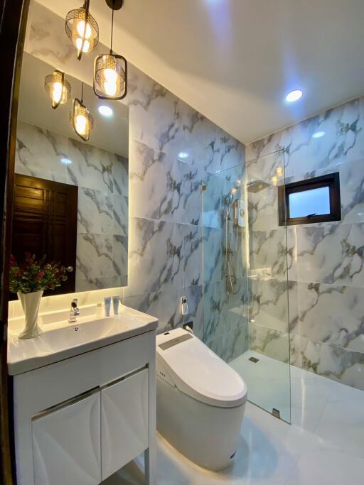 Modern bathroom with marble walls, illuminated mirror, vanity, toilet, and glass-enclosed shower