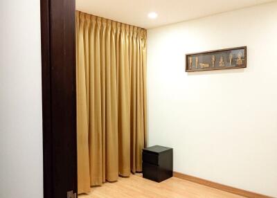 Empty room with wooden flooring, beige curtains, and a small black table