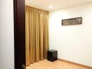 Empty room with wooden flooring, beige curtains, and a small black table