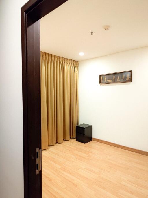 Empty room with wooden flooring, beige curtains, and a small black table