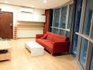 Modern living room with a red sofa, coffee table, wooden flooring, and large windows