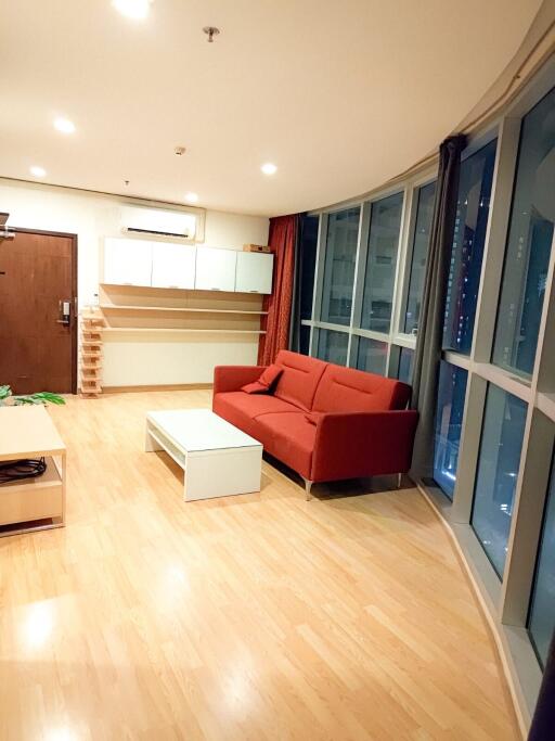 Modern living room with a red sofa, coffee table, wooden flooring, and large windows