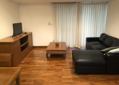 Cozy living room with a black sectional sofa, wooden coffee table, TV on a wooden stand, and dining table chair