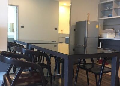 Modern dining area adjacent to a kitchen with a sleek black dining table, four chairs, and a visible refrigerator