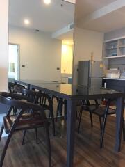 Modern dining area adjacent to a kitchen with a sleek black dining table, four chairs, and a visible refrigerator