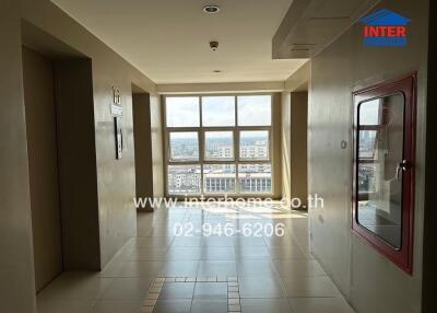 View of a corridor in a building with large windows and an elevator on the left.